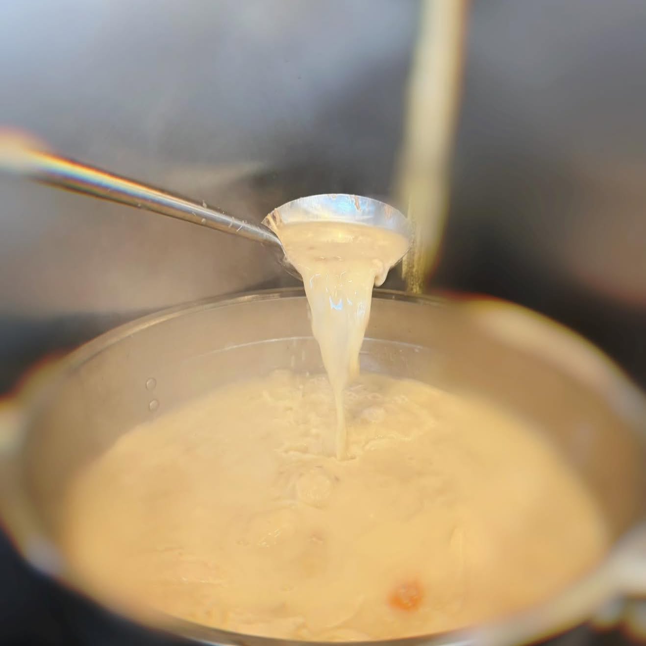 Creamy ramen broth being ladled from the pot