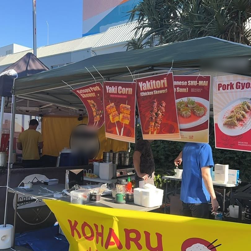The KOHARU market stall under a gazebo with its yellow banner and dish signs